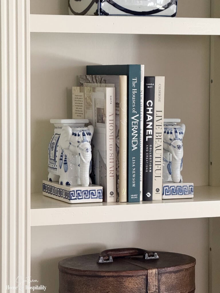 Entertainment center shelf styled with blue and white pottery, books, blue and white elephant bookends.