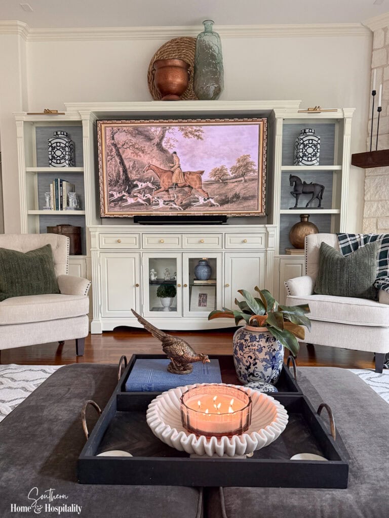 Fall ottoman styling with magnolia leaves, brass pheasant, black tray, marble-look bowl, and candle
