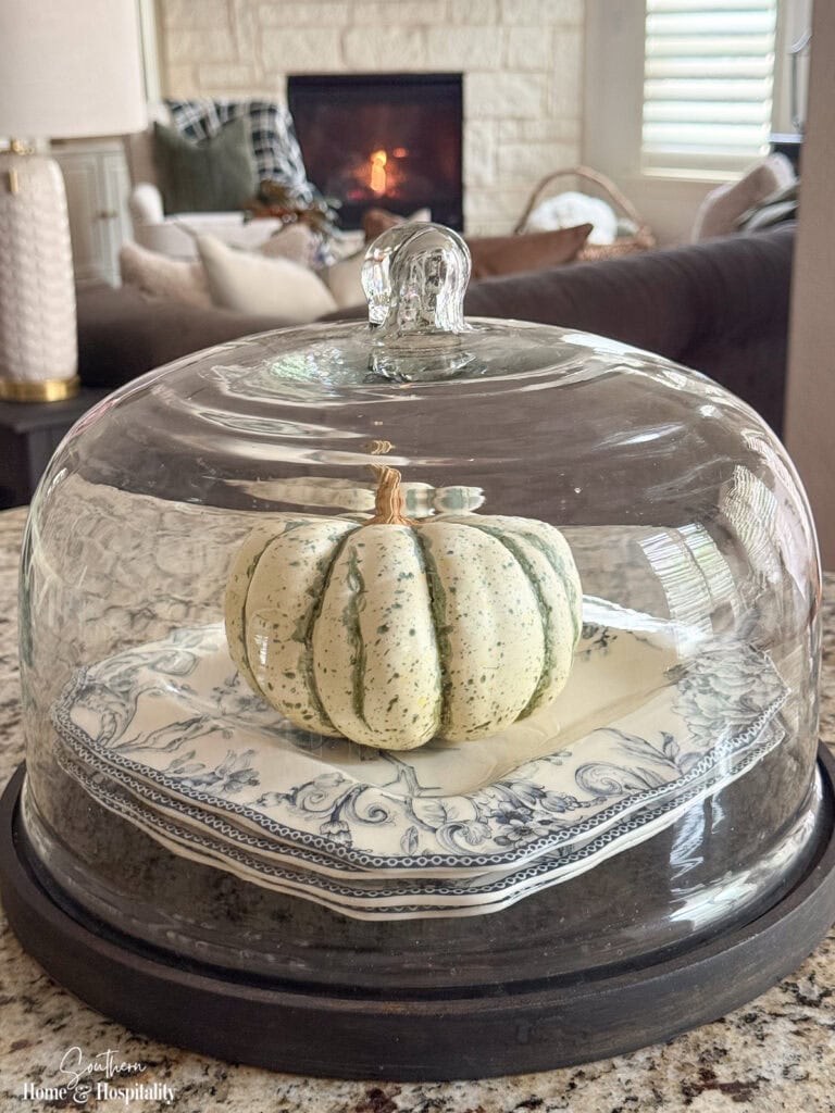 White pumpkin under a glass cloche on stacked blue and white plates for simple fall kitchen decor
