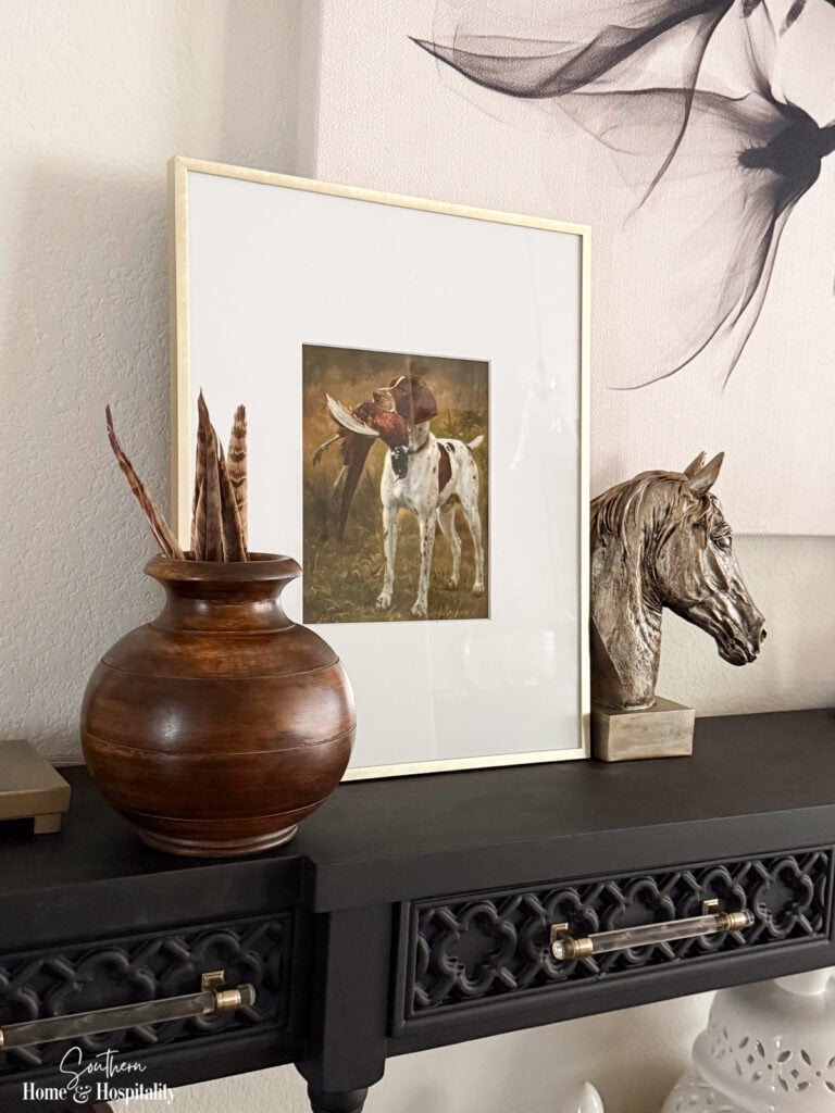Framed hunting print with horse head, warm wood vase, and pheasant feathers on a fall entry table