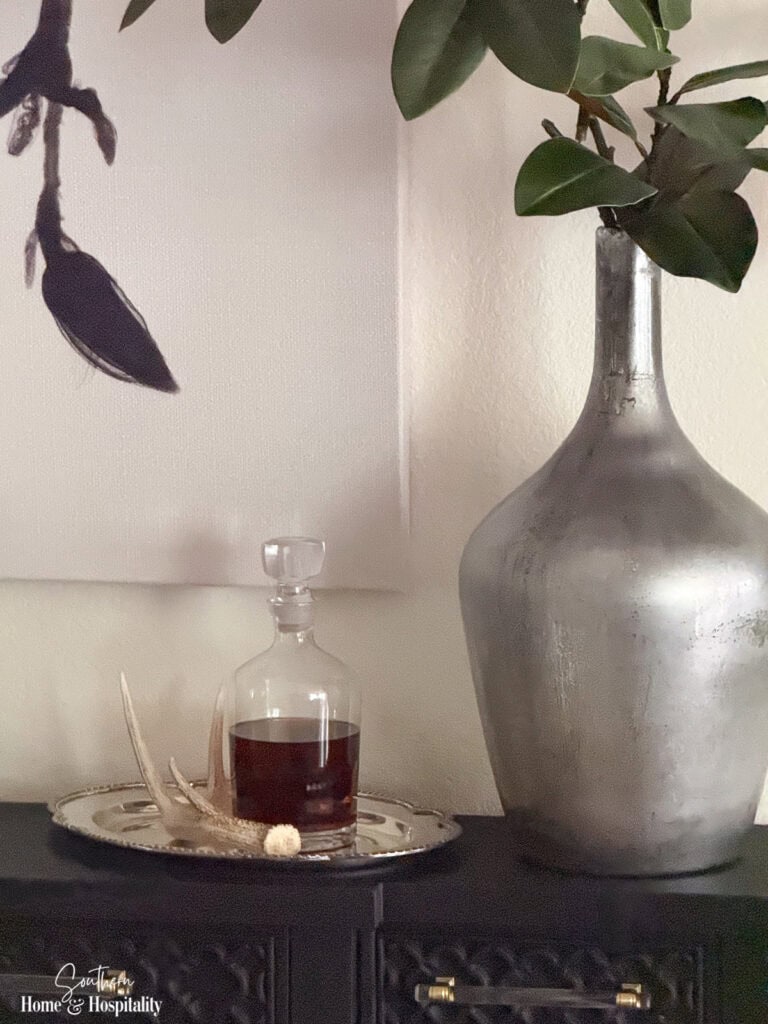 Faux magnolia branches in a silver vase with vintage silver tray, antler, and bourbon decanter