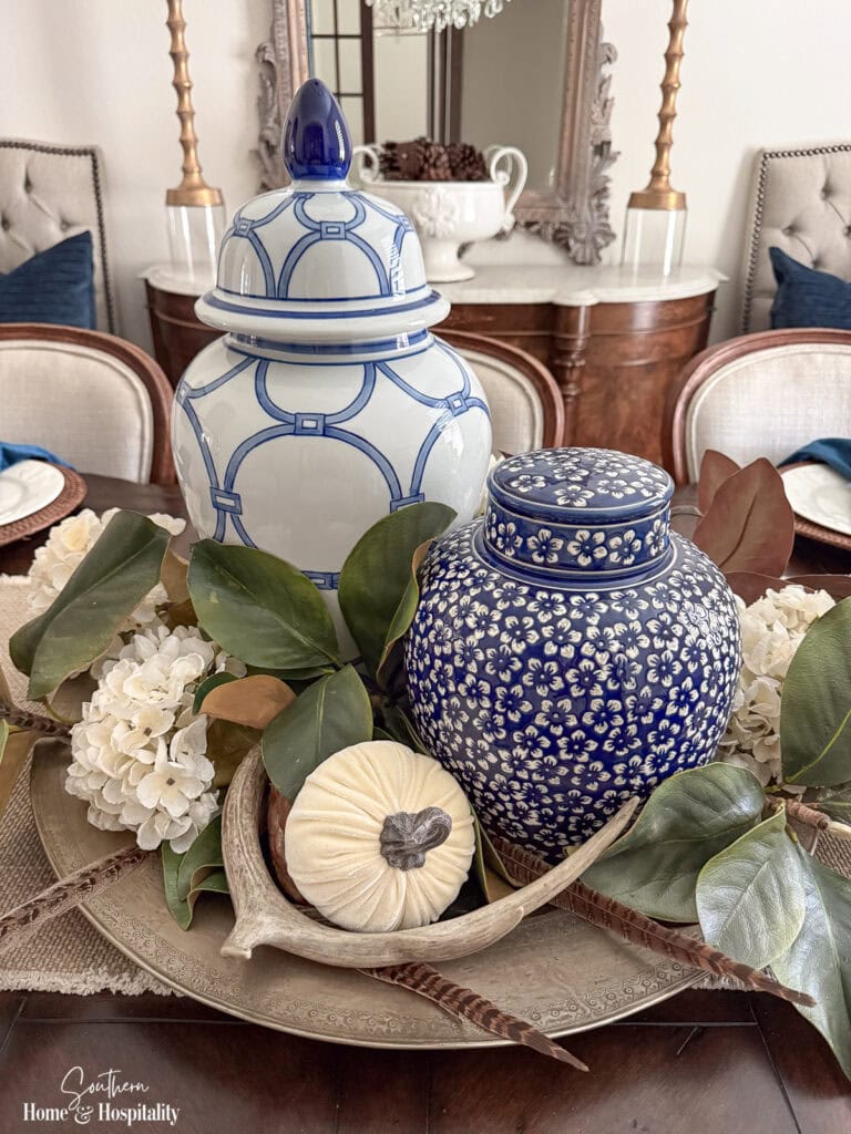 Blue and white fall centerpiece with cream hydrangeas, magnolia leaves, antlers, and pumpkins on an aged brass tray