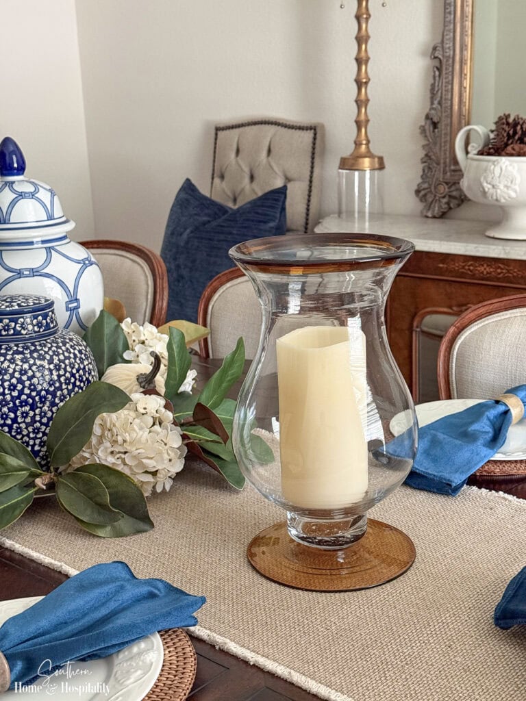 Fall table setting with blue velvet napkin, glass hurricane candle, and traditional blue and white decor