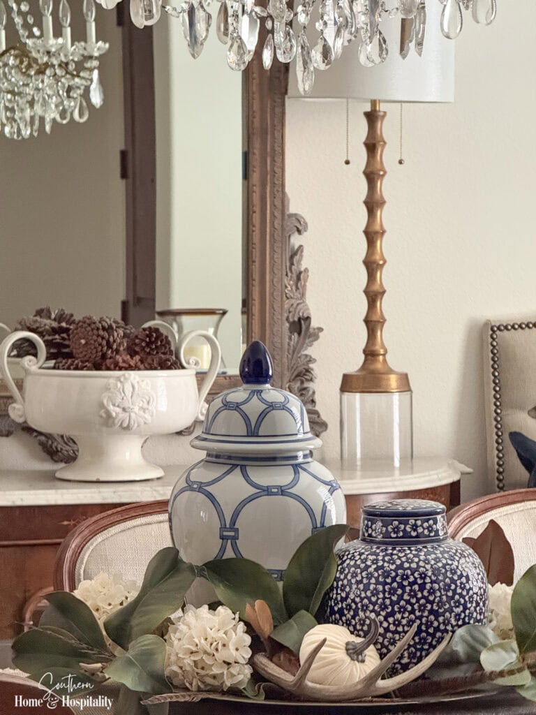 Traditional fall dining room with blue and white table centerpiece, candlelight, dark wood, and cream upholstered chairs