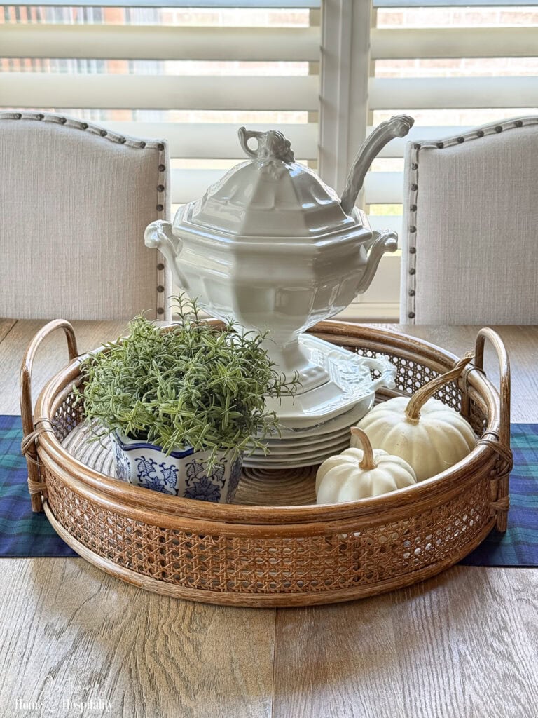 Fall kitchen table centerpiece with white ironstone, blue and white pottery, greenery, and white pumpkins in a rattan tray