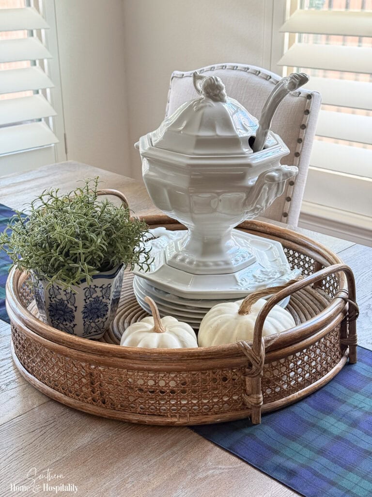 Fall kitchen table with blue and green plaid runner, rattan tray, white ironstone, greenery, and white pumpkins