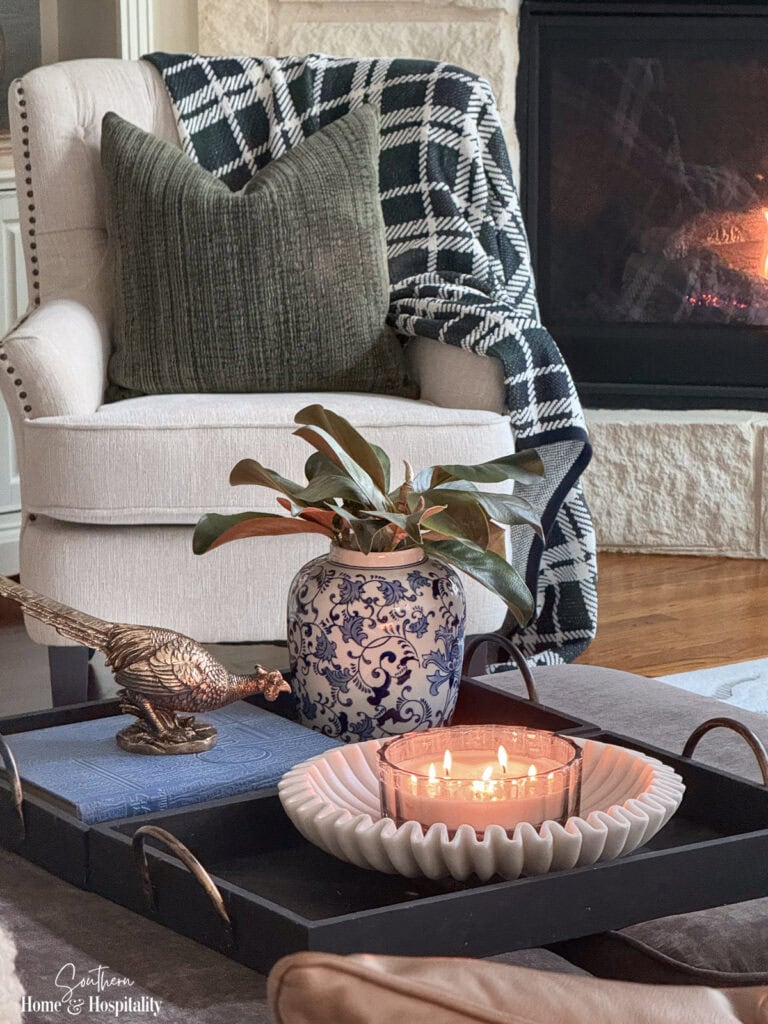 Fall ottoman styling with magnolia leaves, brass pheasant, black tray, marble-look bowl, and candle