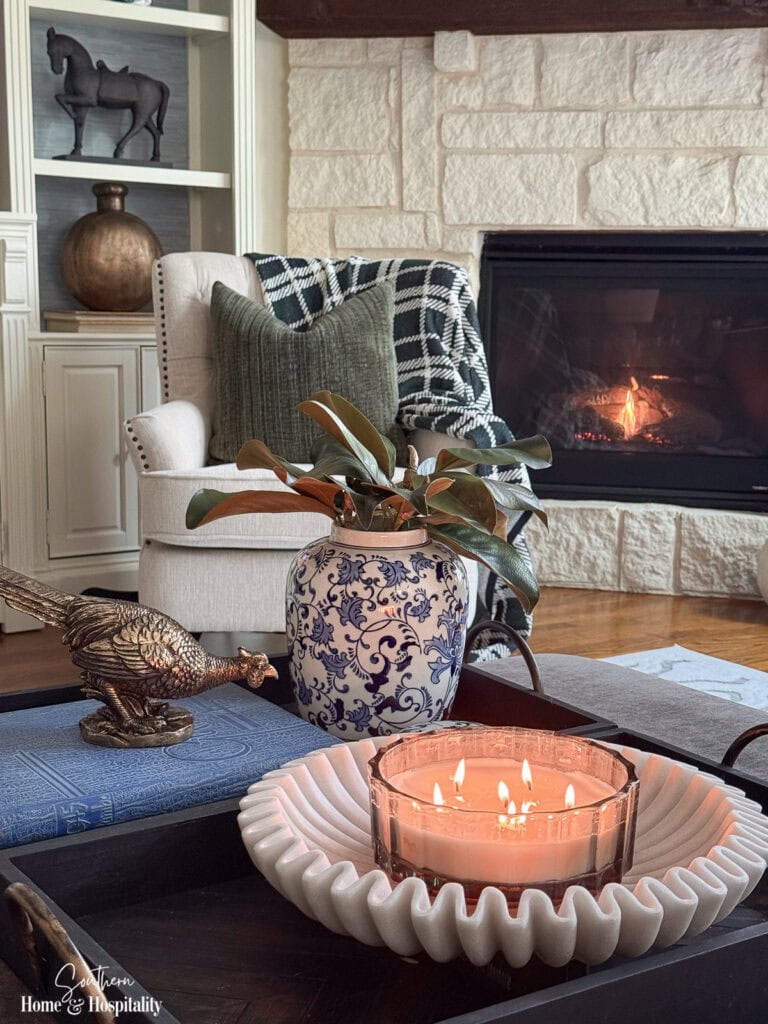 Fall living room ottoman styled with blue and white porcelain, magnolia leaves, brass pheasant, books, and candle