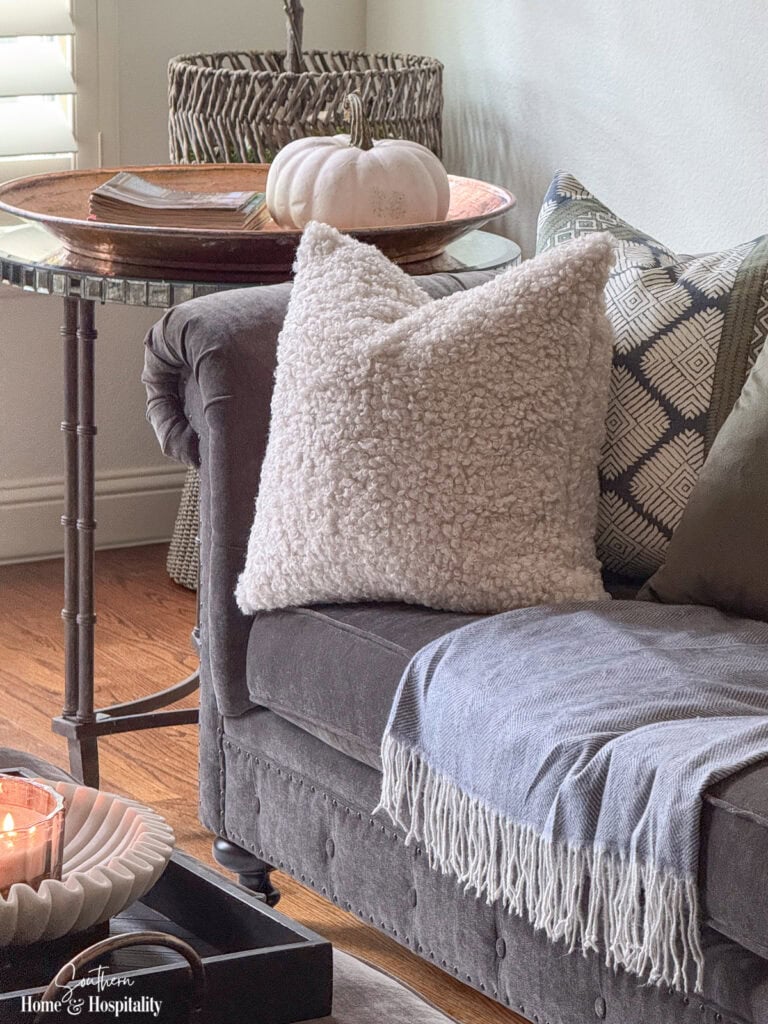 Charcoal velvet sofa with cream bouclé pillow, patterned pillow, and blue herringbone throw for fall