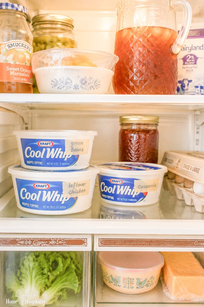 Vintage refrigerator filled with leftovers stored in reused Cool Whip containers, jars of preserves, iced tea, eggs, and other staples.