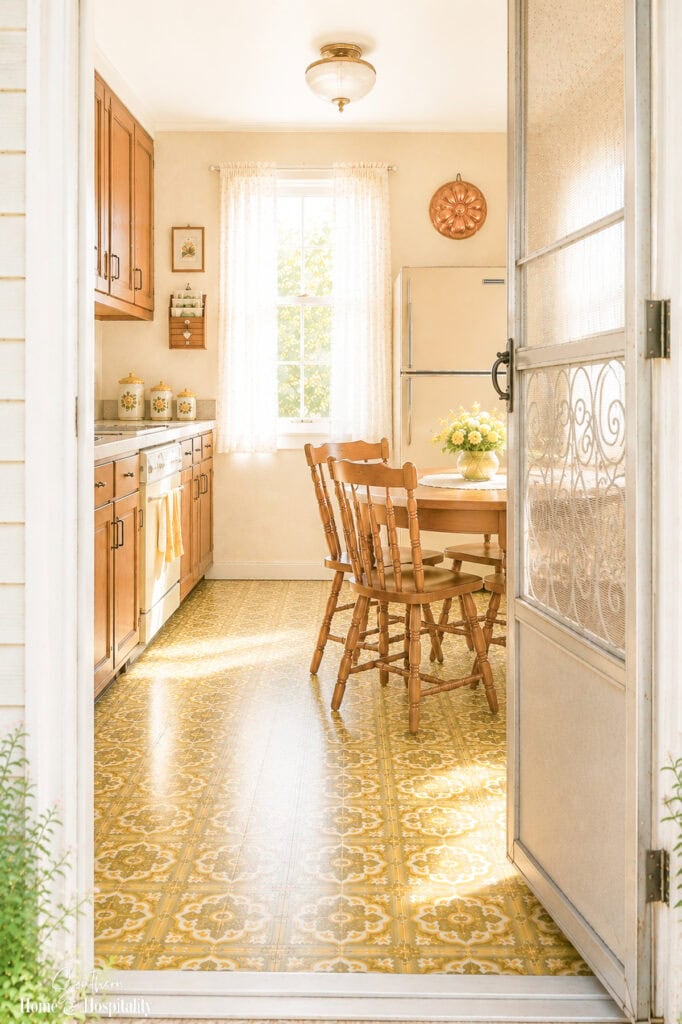 Bright 1970s-style kitchen seen through an open screen door with avocado green and gold flooring and a vintage kitchen table.