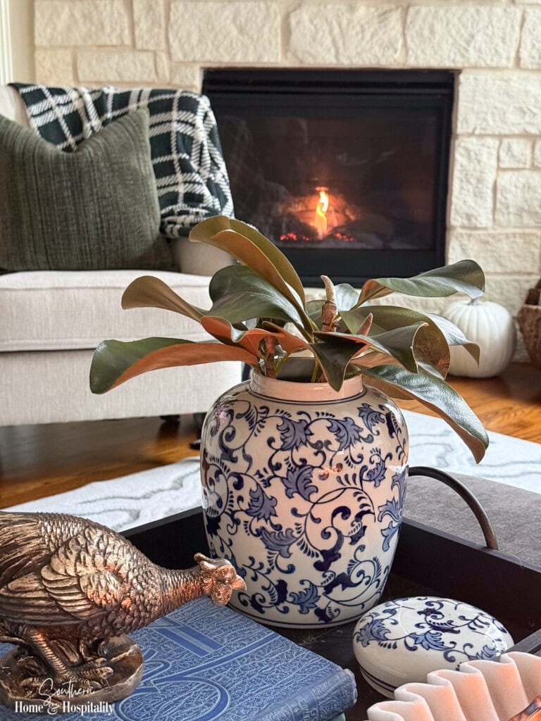 Faux magnolia leaves with green tops and brown undersides arranged in a blue and white vase