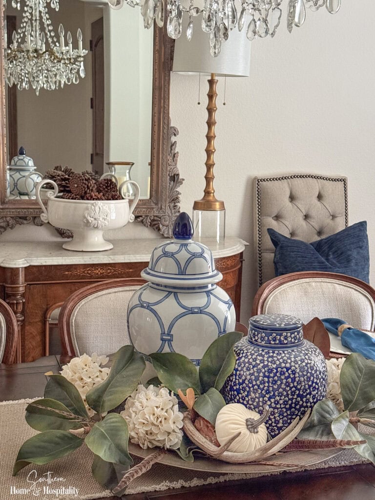 Fall centerpiece with faux magnolia, dried hydrangeas, blue and white pottery, pumpkin, antler, and feathers