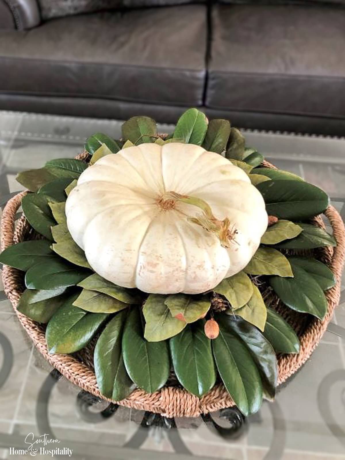 White Cinderella pumpkin surrounded by fresh and faux magnolia leaves in a woven tray