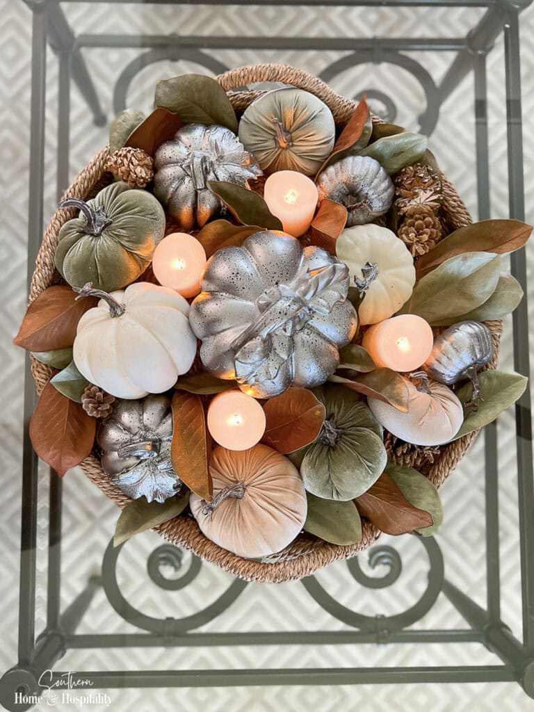 Fall coffee table centerpiece with dried magnolia leaves, velvet pumpkins, pinecones, and candles
