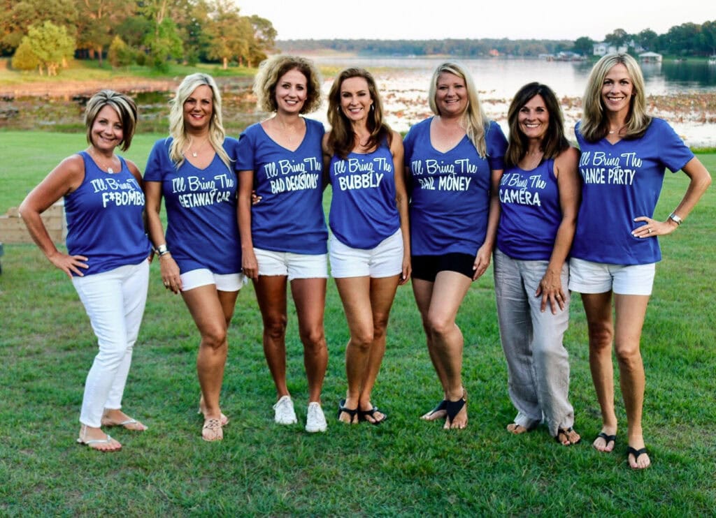 Seven longtime girlfriends in matching blue shirts together by the lake