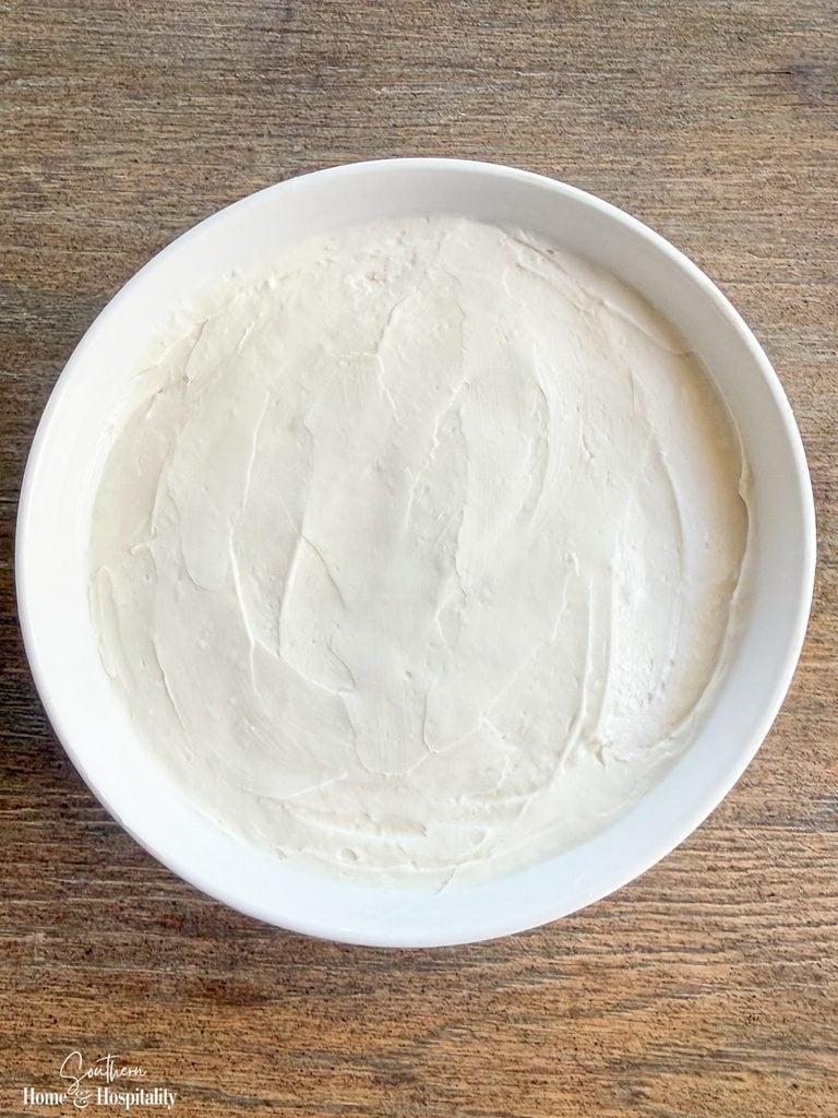 Smooth cream cheese mixture spread evenly in a white serving bowl for caramel apple dip.