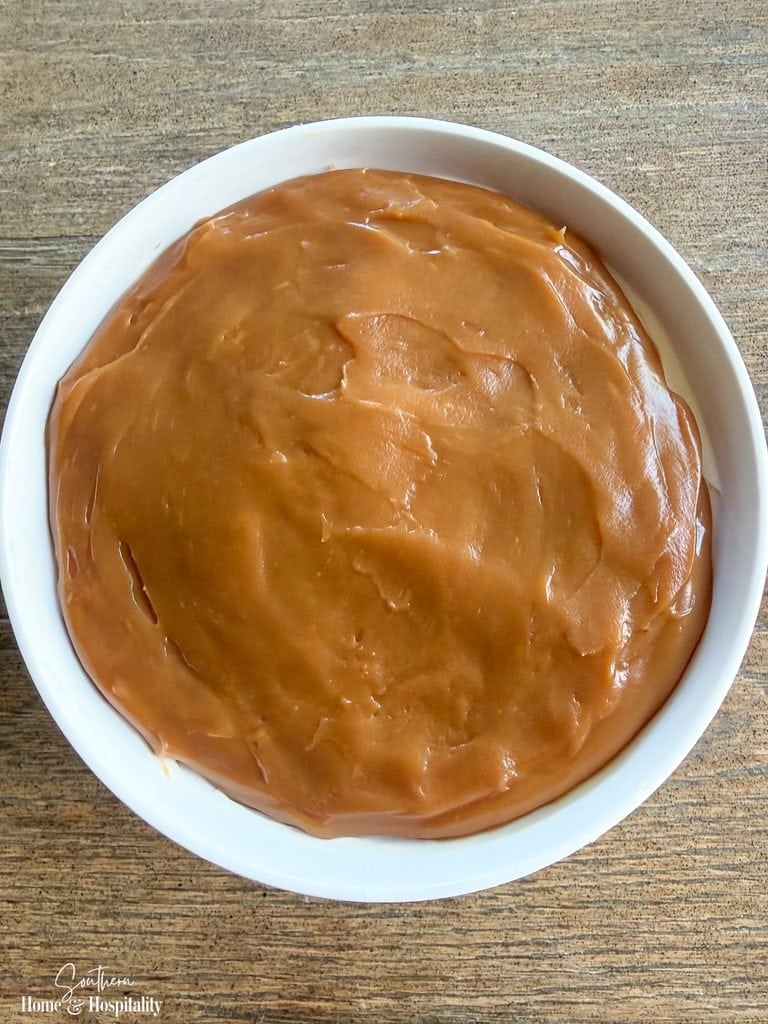 Thick caramel spread over the cream cheese layer in a white bowl.