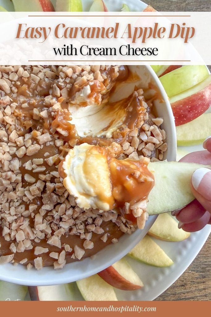 Apple slice topped with cream cheese caramel apple dip and Heath toffee bits, held above a serving bowl surrounded by red and green apple slices.